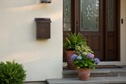 Dark patina vertical copper mailbox on white painted wall with greenery