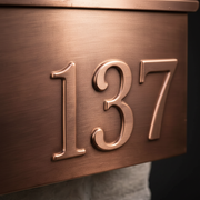 Close-up of brushed copper mailbox showing hand-finished metallic grain and embossed house numbers